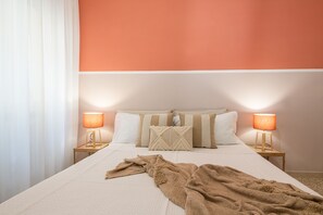 Una cama bien hecha con una manta color beige, dos lámparas de noche y un cojín con diseño geométrico.