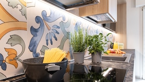 A kitchen with a black induction cooktop, a pot of spaghetti, and two potted plants on the counter. - Renzi 23 - Two Bedroom Apartment, Sleeps 6 (Cattolica)
