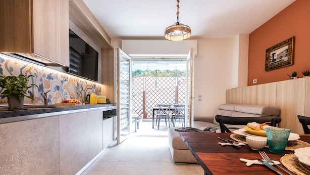 A modern kitchen with a dining area, a wooden table set with plates, bowls, and cutlery, and a view of the outdoor patio. - Renzi 23 - Two Bedroom Apartment, Sleeps 6 (Cattolica)