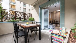 A dining area with a wooden table and chairs, a decorative metal fence, and a view of a building in the background. - Renzi 23 - Two Bedroom Apartment, Sleeps 6 (Cattolica)