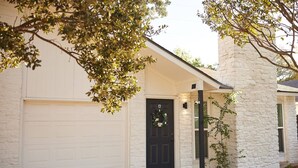 A house with a white garage door, a black front door with a wreath, and a stone pillar. - 2BR Ensuite | Near UT & The Domain (Austin)