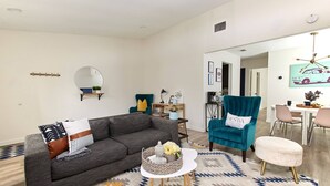 A modern living room with a grey sofa, teal armchair, and a small round table with a basket. - 2BR Ensuite | Near UT & The Domain (Austin)