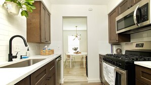 A modern kitchen with dark wooden cabinets, a stainless steel stove, a microwave, and a sink. - 2BR Ensuite | Near UT & The Domain (Austin)