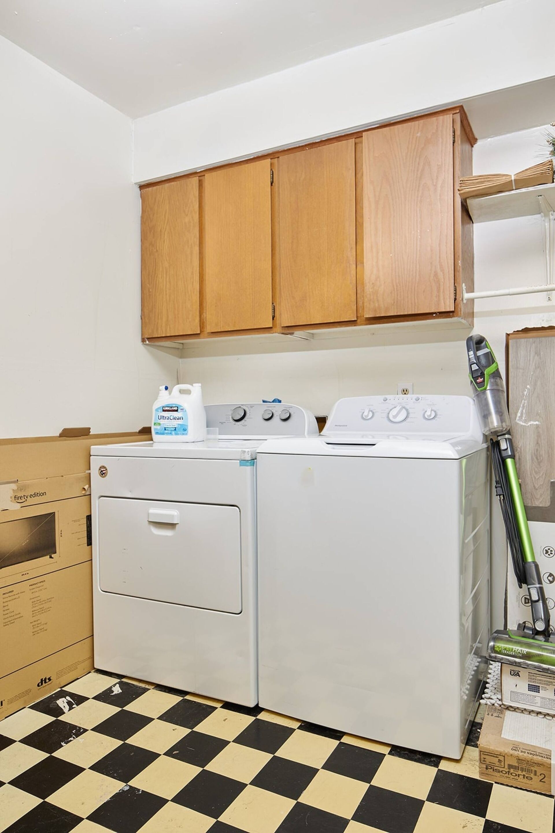 Un espace buanderie comprenant un lave-linge, un sèche-linge, des armoires en bois et un balai.
