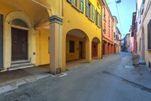A narrow street with yellow buildings, arched doorways, and a clear sky.