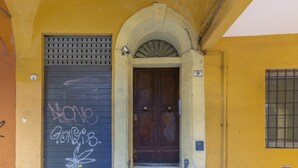 Une entrée d’immeuble avec une porte à volets fermés, une plaque indiquant le numéro de l’immeble et une petite fenêtre grillagée.