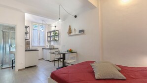 Une pièce de taille modeste comprenant un lit, un bureau, une chaise, une petite table et un coin cuisine.