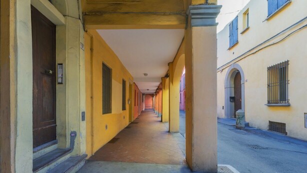 Un couloir aux murs jaunes, doté d’un sol carrelé, et donnant sur une rue d’un côté.