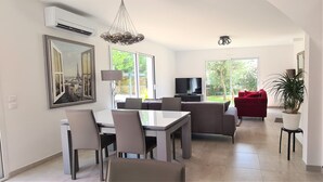 Ein modernes Wohnzimmer mit Essbereich, großen Fenstern und einem Fernseher.
