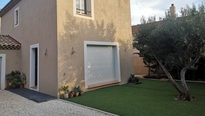 Ein zweistöckiges Haus mit Ziegeldach, einer Garagentür und einem kleinen Rasen mit Topfpflanzen.