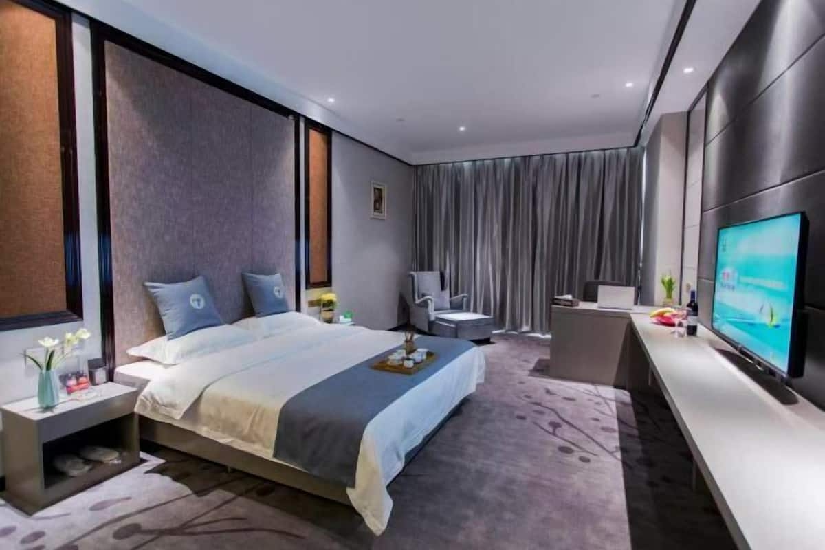 Una habitación de hotel moderna con una cama grande, un escritorio, una silla, un televisor y una ventana con cortinas.