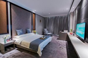 Una habitación de hotel moderna con una cama grande, un escritorio, una silla, un televisor y una ventana con cortinas.