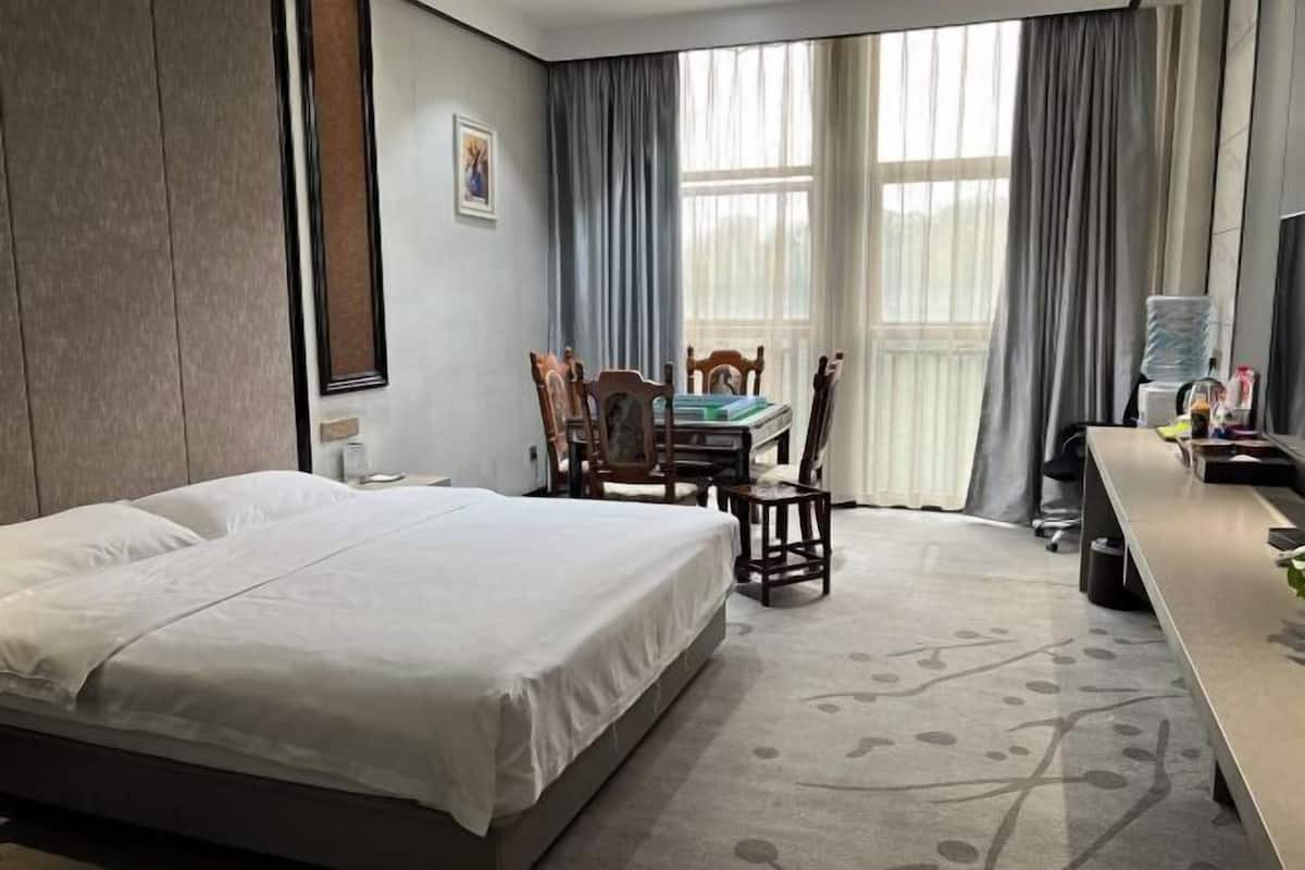 Una habitación de hotel con cama, escritorio, silla y ventana con cortinas.