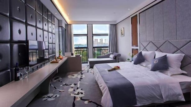 A modern hotel room with a large bed, a seating area with a view, and a wall of storage cubes. - Yuting Impression Hotel (Zhongjiang)