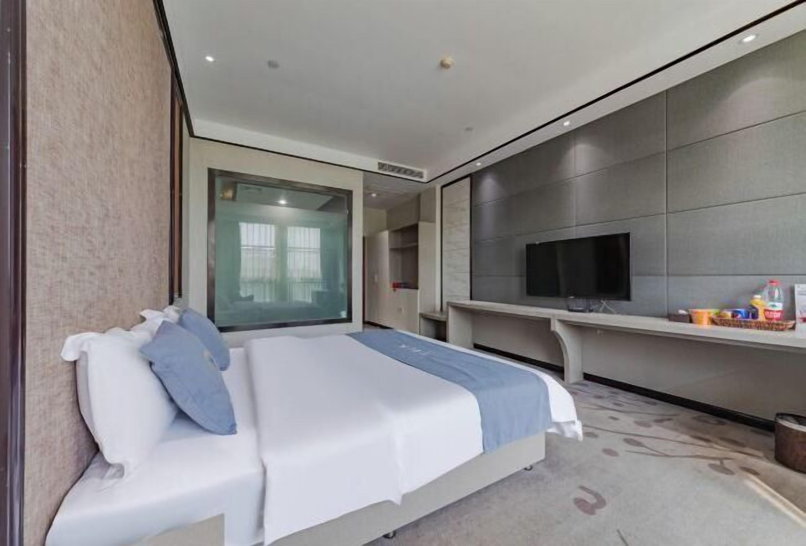 A modern hotel room with a bed, a TV, and a large window.