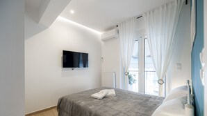 A bedroom with a bed, a flat-screen TV mounted on the wall, and a window with curtains.