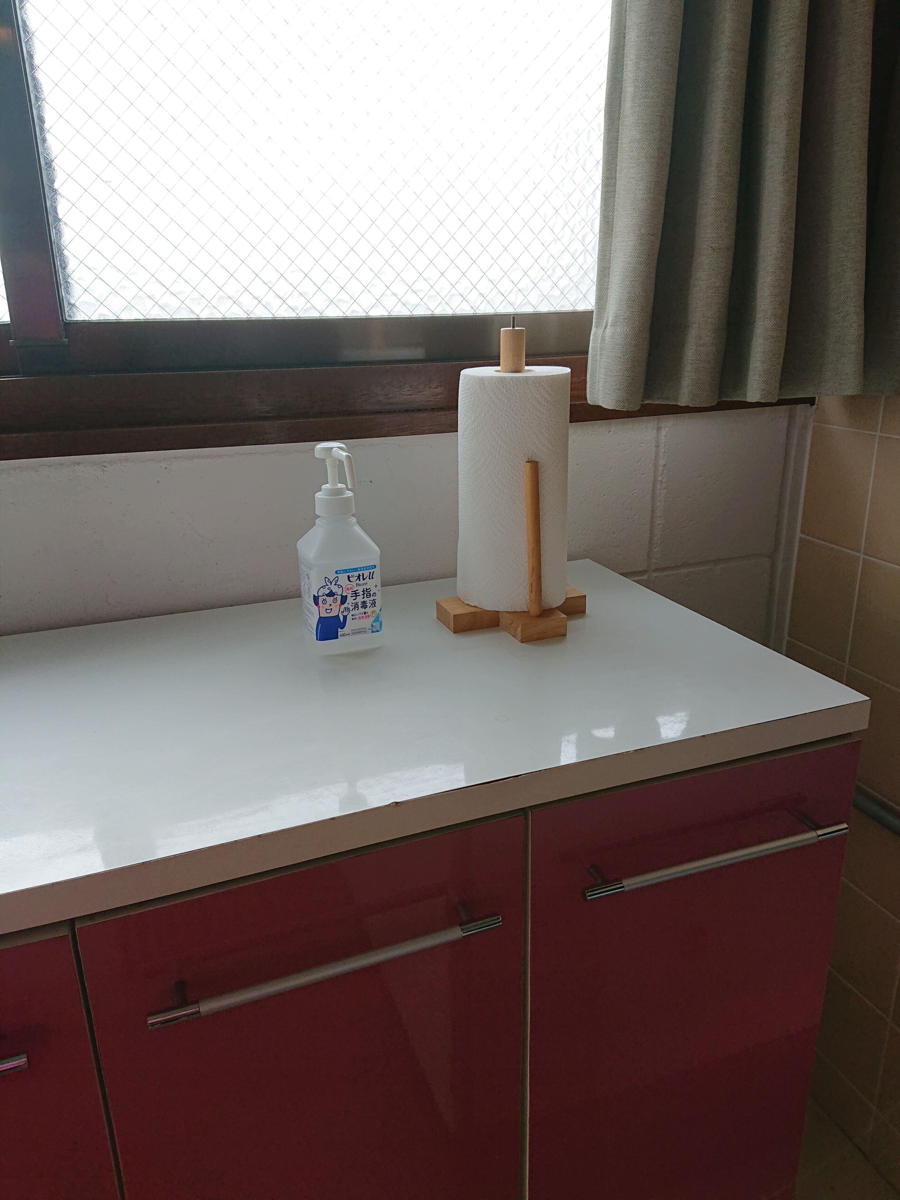 Un baño con encimera blanca, una botella de desinfectante de manos, un rollo de papel higiénico y un palito de madera.