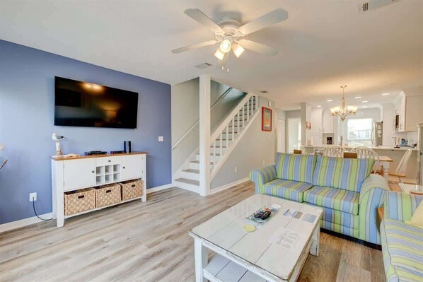 A living room with a TV, white entertainment unit, striped sofa, and a ceiling fan.