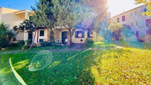 A courtyard with a large tree, a white table, and a building with multiple windows. - L'avru Di La Canna La Cinta (San Teodoro)