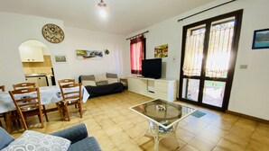 A living room with a sofa, a glass coffee table, a TV, and a dining area with chairs and a table. - L'avru Di La Canna La Cinta (San Teodoro)