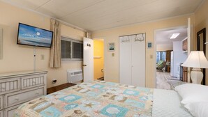 Ein Hotelzimmer mit einem großen Bett, einem an der Wand befestigten Fernseher, einem Schminktisch und einer Tür zu einem weiteren Raum.