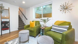 A living room with two green armchairs, a white ottoman, a small table with a vase, and a staircase. - Bright and Modern Basement Apartment ✿ DT Neighborhood (Vancouver)