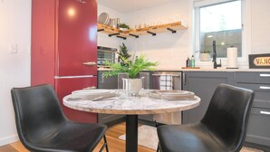 A modern kitchen with a red refrigerator, a round marble table with two black chairs, and a window with a view of the outdoors. - Bright and Modern Basement Apartment ✿ DT Neighborhood (Vancouver)