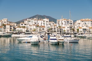 A marina with boats docked, surrounded by white buildings with red-tiled roofs, and a mountain in the background. - Luxury 3BD in Aldea Blanca, Pool & Puerto Banús (Marbella)