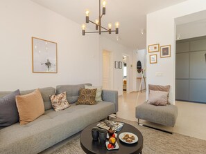 Un soggiorno moderno con un divano grigio, una poltrona grigia più piccola, un tavolino da caffè con una rivista e degli snack, e un lampadario.