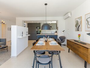 Una cucina moderna con zona pranzo, con un tavolo in legno apparecchiato per quattro persone, sedie grigie e una lampada a sospensione sopra.