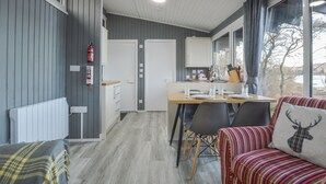 Een moderne kamer met een eethoek, een bank met een gestreept kussen en uitzicht op bomen.