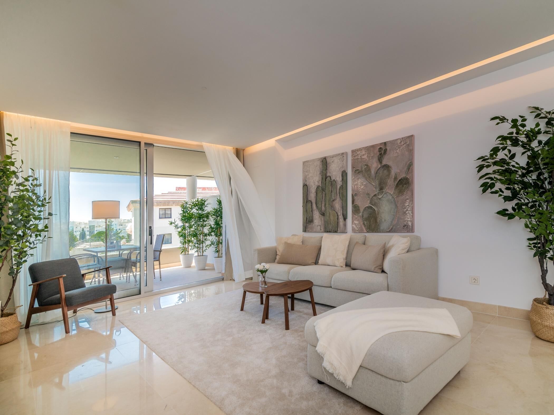 Uma sala de estar moderna com sofá, poltrona e mesa de centro, uma janela grande com vista e duas pinturas penduradas na parede.