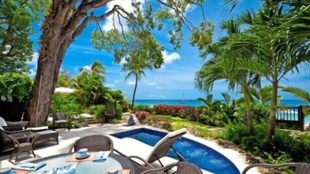 A poolside area with lounge chairs and a table, surrounded by lush greenery and a view of the ocean. - 1 bedroom Beachfront Condo, small pool, gorgeous sea view (Paynes Bay)