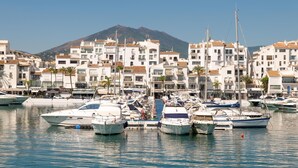 Un port de plaisance où sont amarrés des bateaux, entouré de bâtiments blancs aux toits recouverts de tuiles rouges, avec une montagne en arrière-plan.