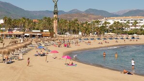 Une plage avec des transats, des parasols et une statue.
