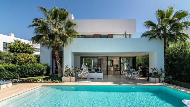 A modern house with a swimming pool, outdoor seating, and lush landscaping.