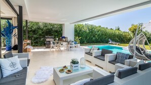 A spacious outdoor living area with a pool, wicker furniture, and a grill.