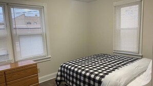 Ein Schlafzimmer mit Bett, Kommode und zwei Fenstern mit Jalousien.