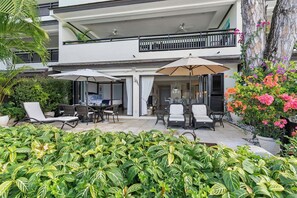 Un bâtiment à deux étages doté d’un balcon, d’un espace extérieur aménagé avec des chaises et des tables, et agrémenté de diverses plantes.