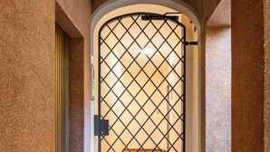 Un couloir avec un mur à texture, une grille métallique et un sol carrelé.