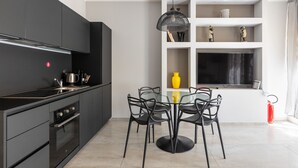 Une cuisine moderne avec des meubles de rangement aux couleurs sombres, une table à manger avec des chaises et une étagère intégrée pour la télévision.