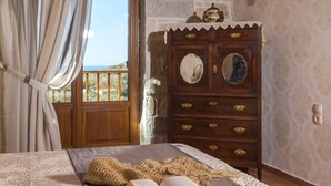 Un dormitorio con un aparador de madera, una cama con una manta texturizada y vista al mar a través de una ventana.