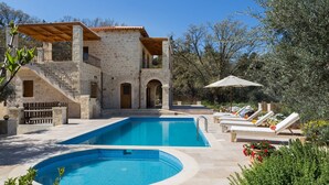 Una villa de piedra con piscina, mobiliario exterior y jardín.