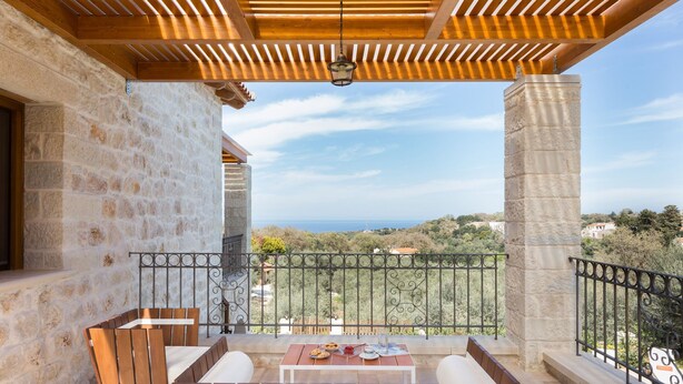 Un balcón con una pérgola de madera, columnas de piedra y vista al mar.