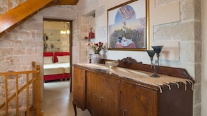 Una escalera de madera conduce a un dormitorio con cabecera roja, un aparador de madera con un florero y un cuadro en la pared.