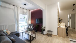 A modern living room with a grey sofa, a coffee table, and a TV mounted on a purple wall. - Calliope (Athenian apartment close to the center) (Athens)