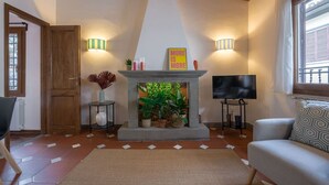 Un salon chaleureux avec une cheminée, deux lampes fixées au mur, un téléviseur et un canapé confortable.