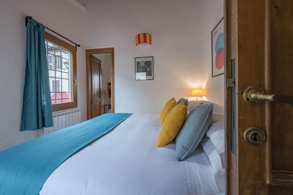 Ein Schlafzimmer mit einem Bett, einem Fenster mit Vorhängen, einer Tür und einer Wandlampe.