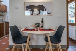 A dining area with a round table, two chairs, a framed animal silhouette, a bottle, and glasses. - Neri Apartment in Florence (Firenze)