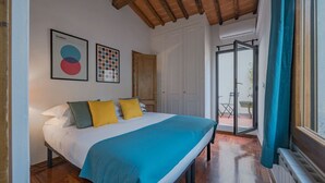 A bedroom with a bed, a wooden ceiling, a door, and a view through a window.